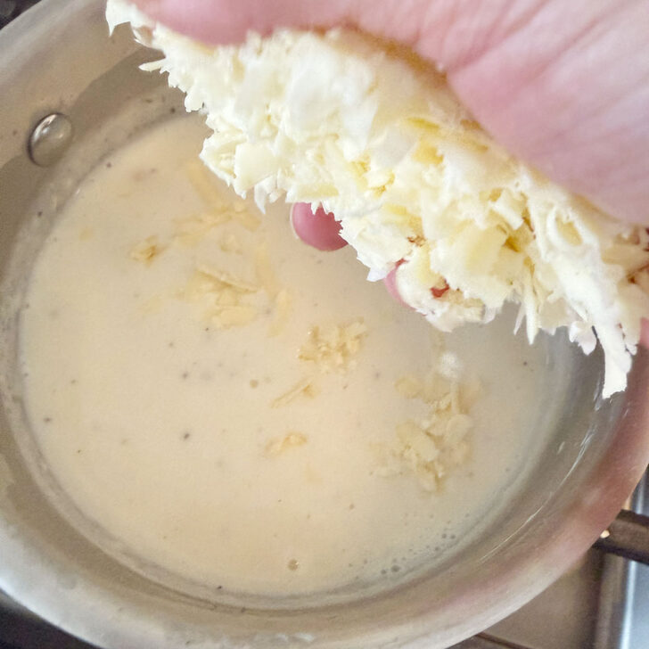 Adding shredded cheese to the white sauce.