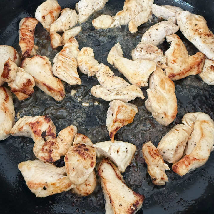 Chicken breast pieces browning in a skillet.