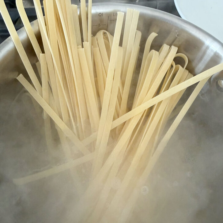 Fettuccine added to a pot of boiling water.