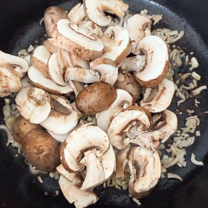 Shallots and mushrooms cooking in a skillet.