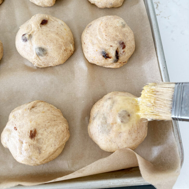 Brushing the buns with an egg wash.