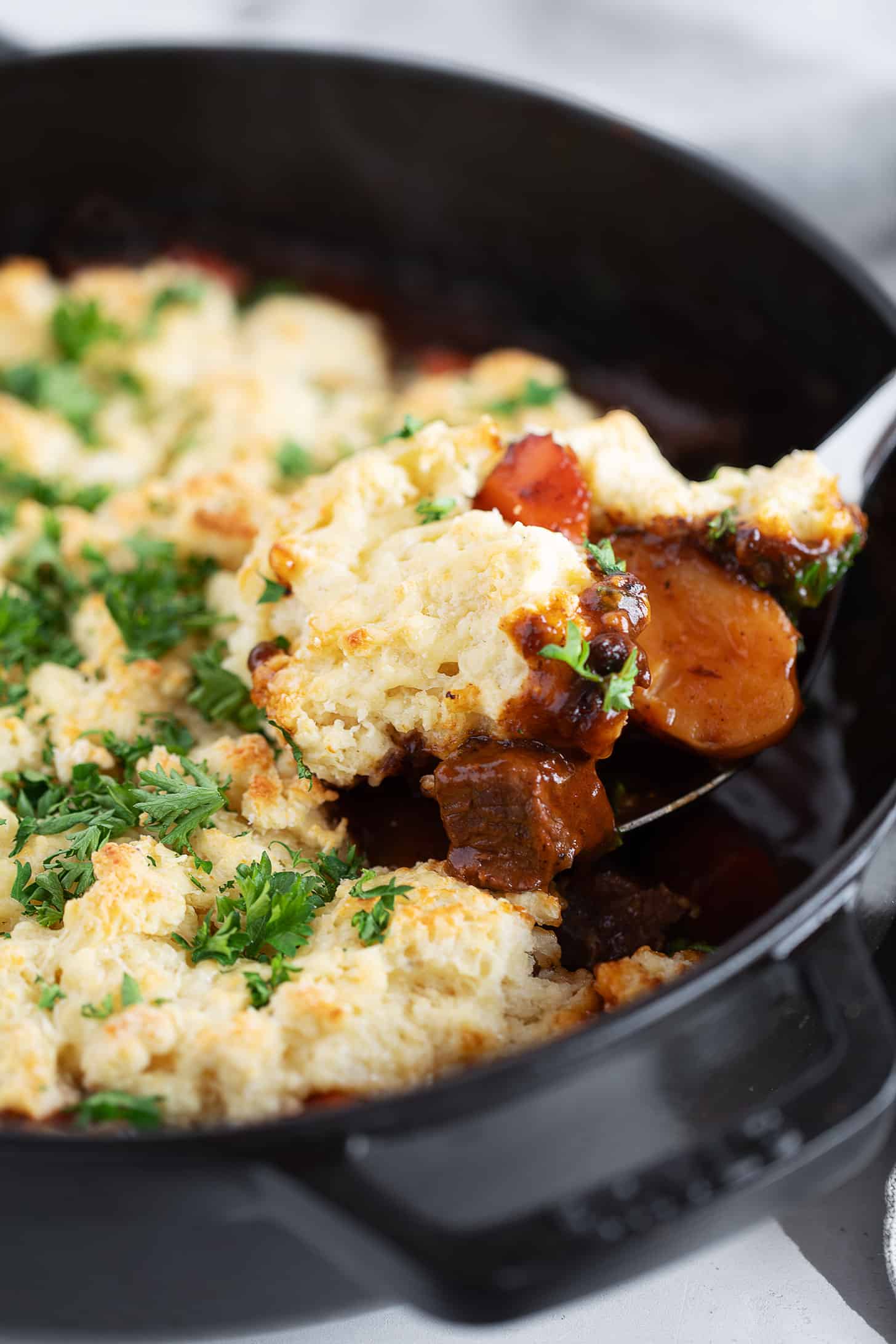 Guinness beef stew with a biscuit topping being spooned out.