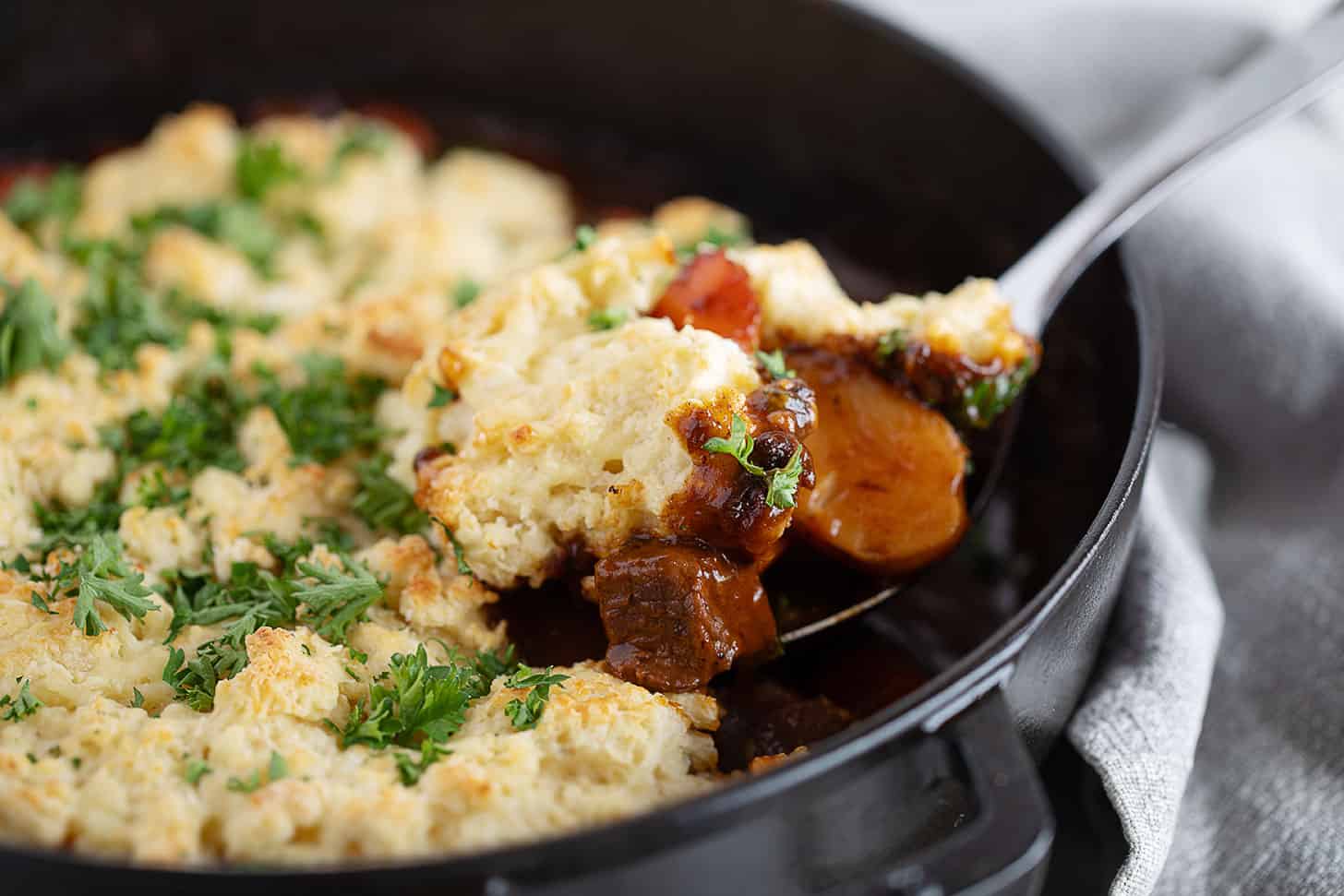 Guinness beef stew with a biscuit topping being spooned out.