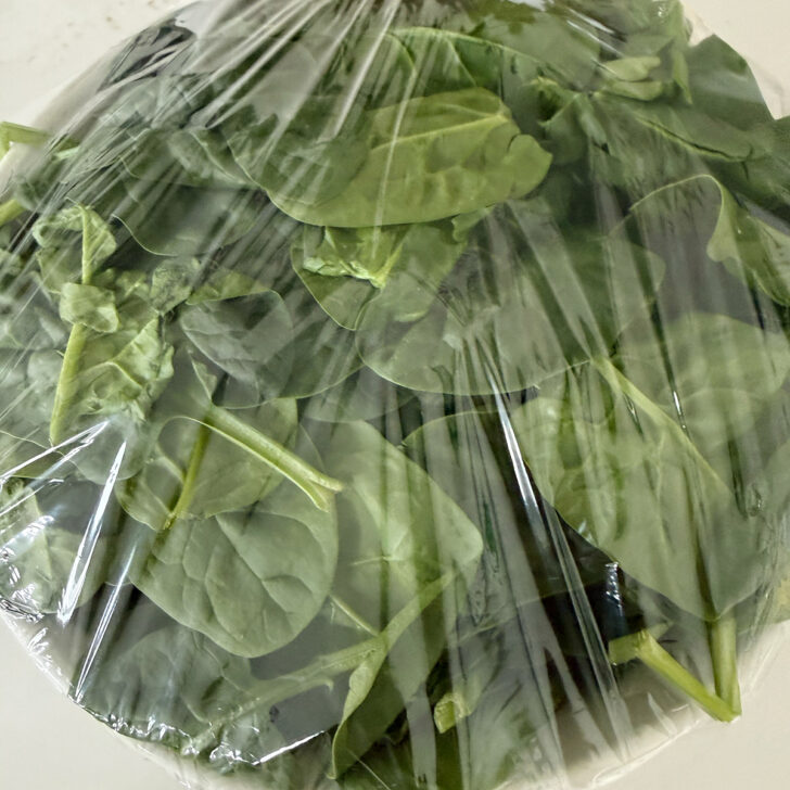 Spinach in a plastic-covered bowl before microwaving,