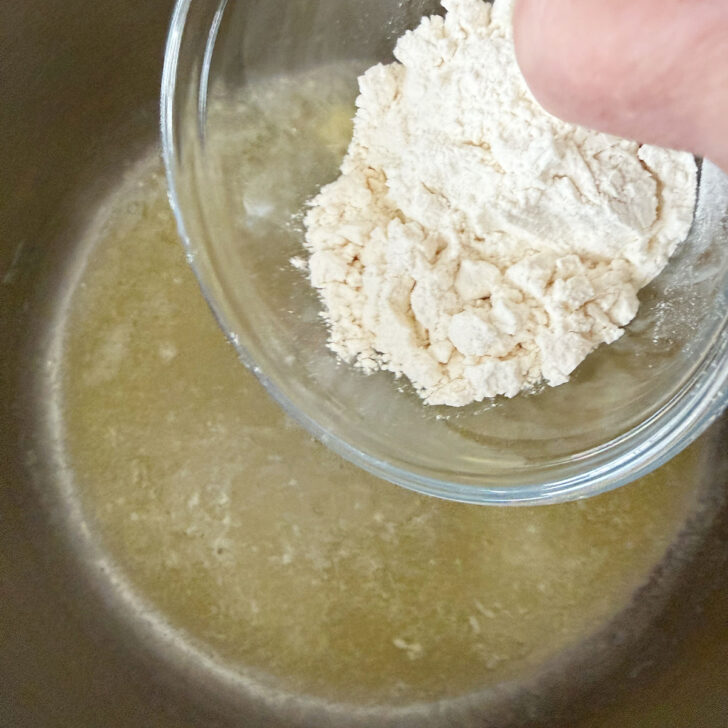 Adding flour to melted butter in a saucepan.