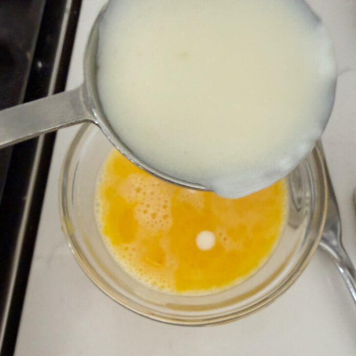 Adding hot milk mixture to the eggs in a small bowl.