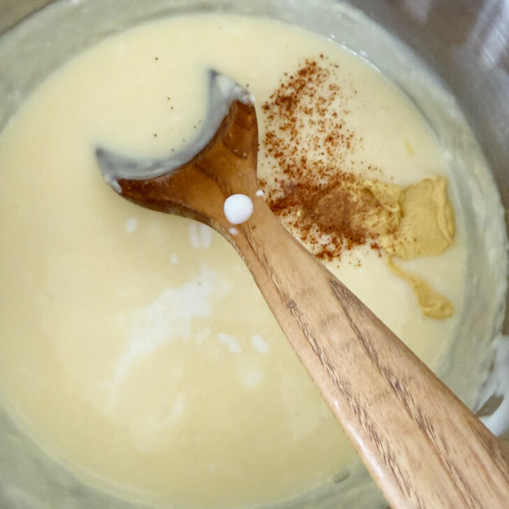 Adding seasoning to the white sauce in the saucepan.