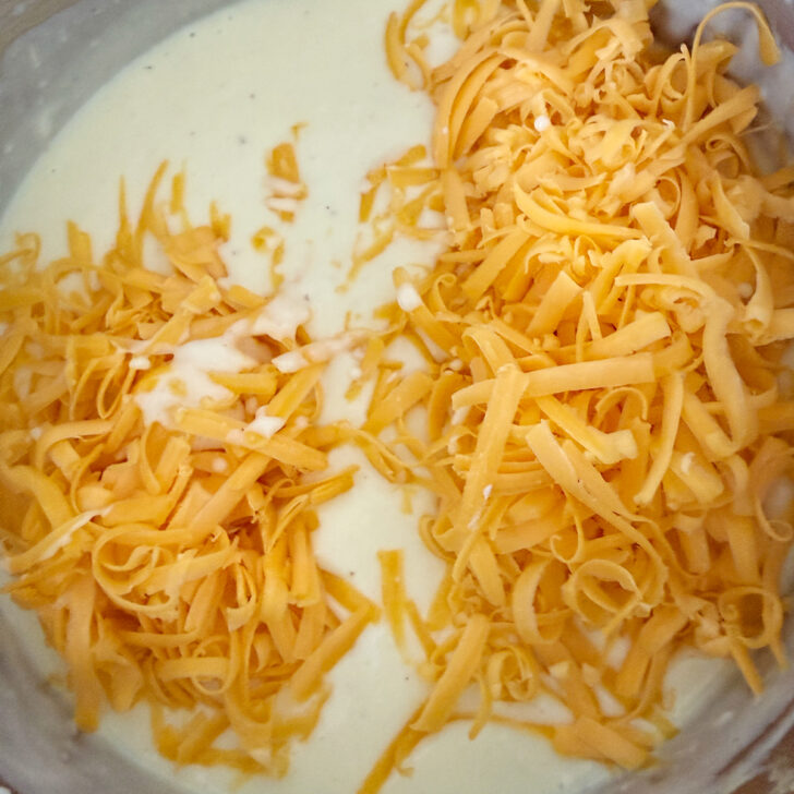 Adding shredded cheese to the white sauce in the saucepan. 