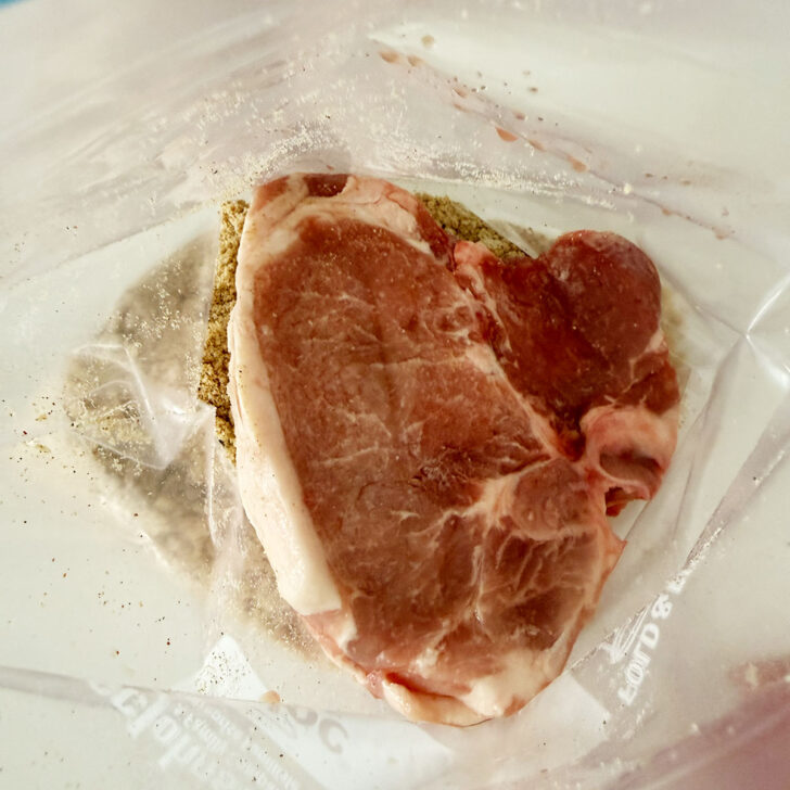 Adding pork chops to a plastic bag with the homemade shake and bake.