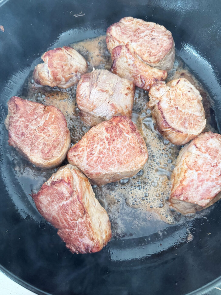 Searing the pork medallions in a hot skillet.
