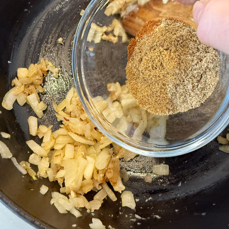 Adding the spices to the softened onion in a skillet.