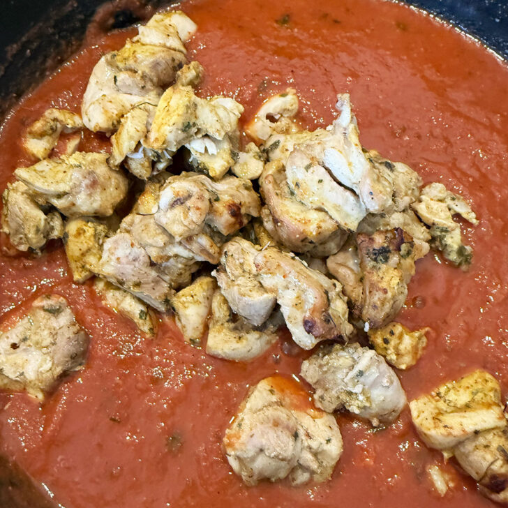 Chicken pieces added to the tomato gravy in the skillet.