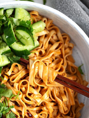 Spicy Málà noodles in a serving bowl with smashed cucumber and cilantro.