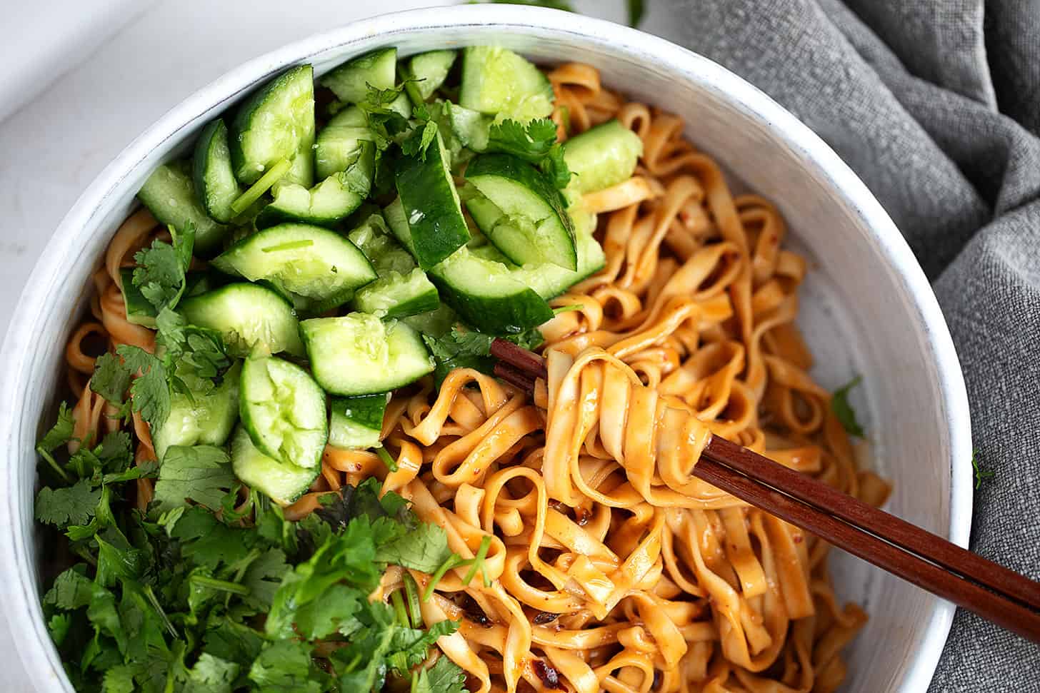 Spicy Málà noodles in a serving bowl with smashed cucumber and cilantro.