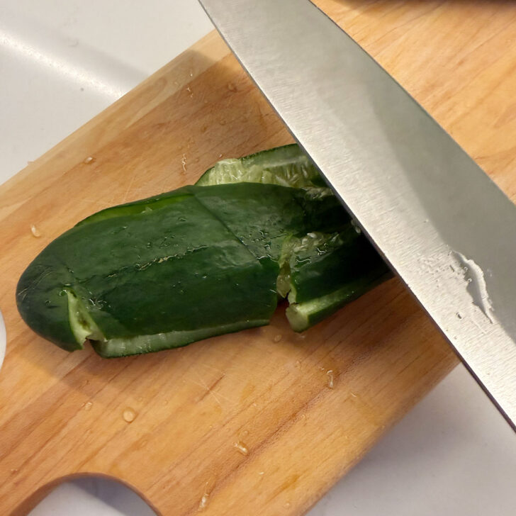 Smashing a mini cucumber with a knife.