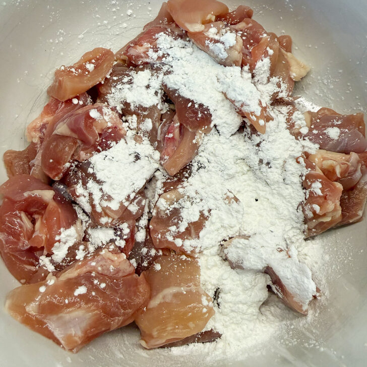 Coating chicken pieces in cornstarch before cooking.