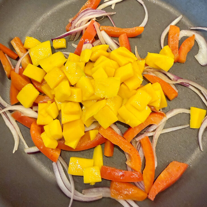 Onion, bell pepper and mango chunks in a skillet.