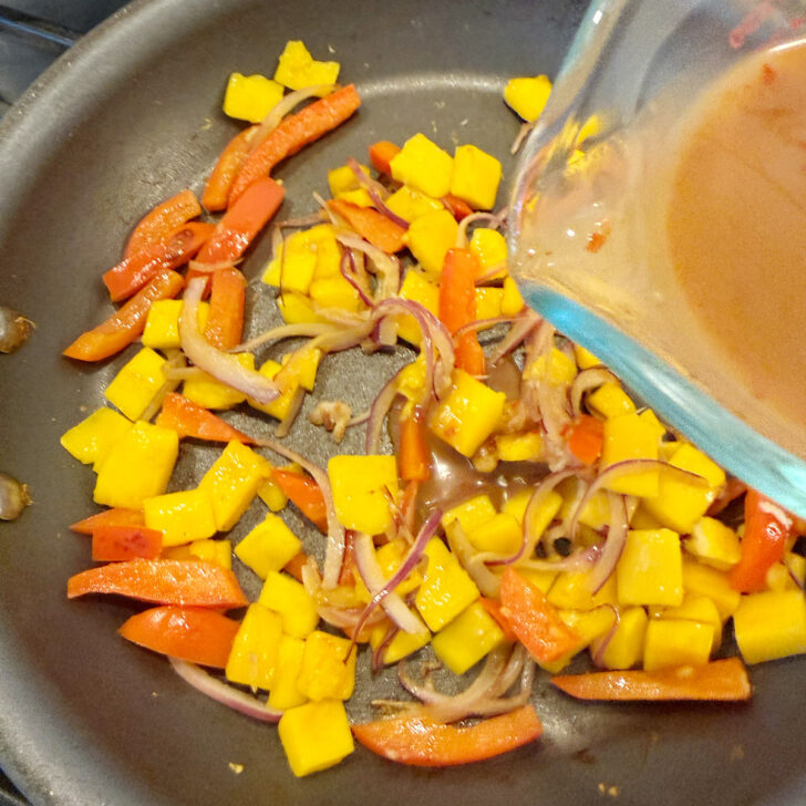 Adding the stir fry sauce to the skillet with the vegetables and mango,