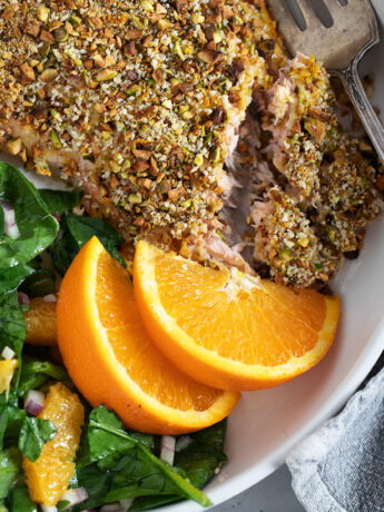 Pistachio-crusted salmon with orange on a plate with an orange salad.