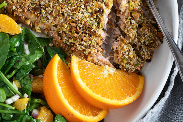 Pistachio-crusted salmon with orange on a plate with an orange salad.