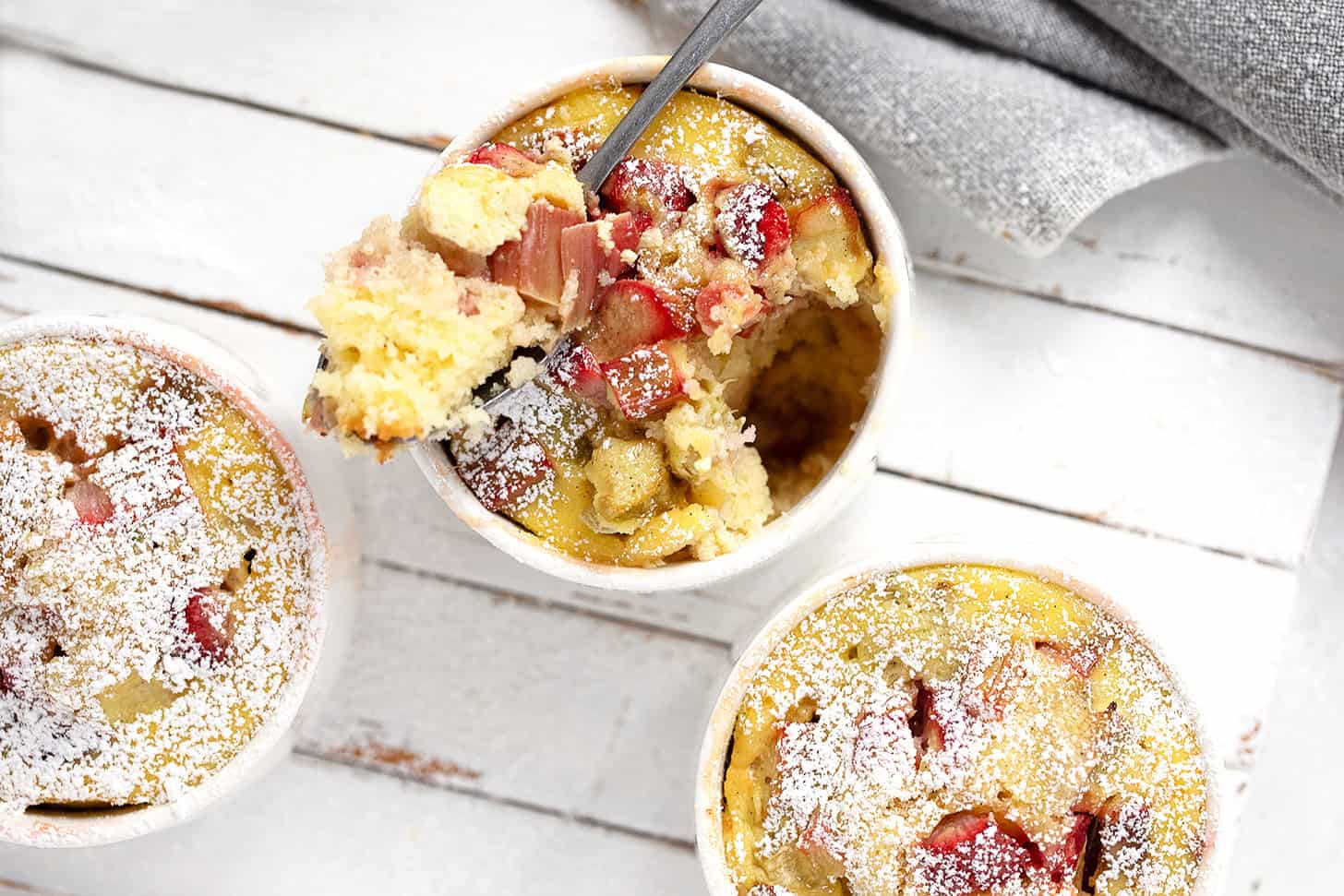 Rhubarb custard cake cups on a serving board with a spoon.
