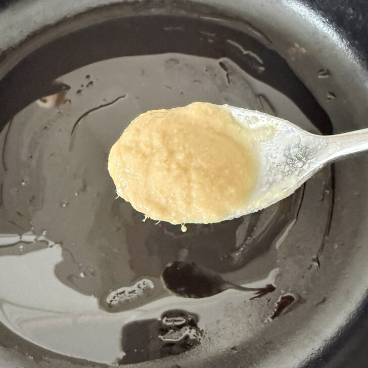 Adding ginger garlic sauce to a skillet with oil.