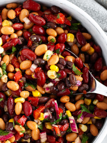 Mexican bean salad in a bowl with a large spoon.