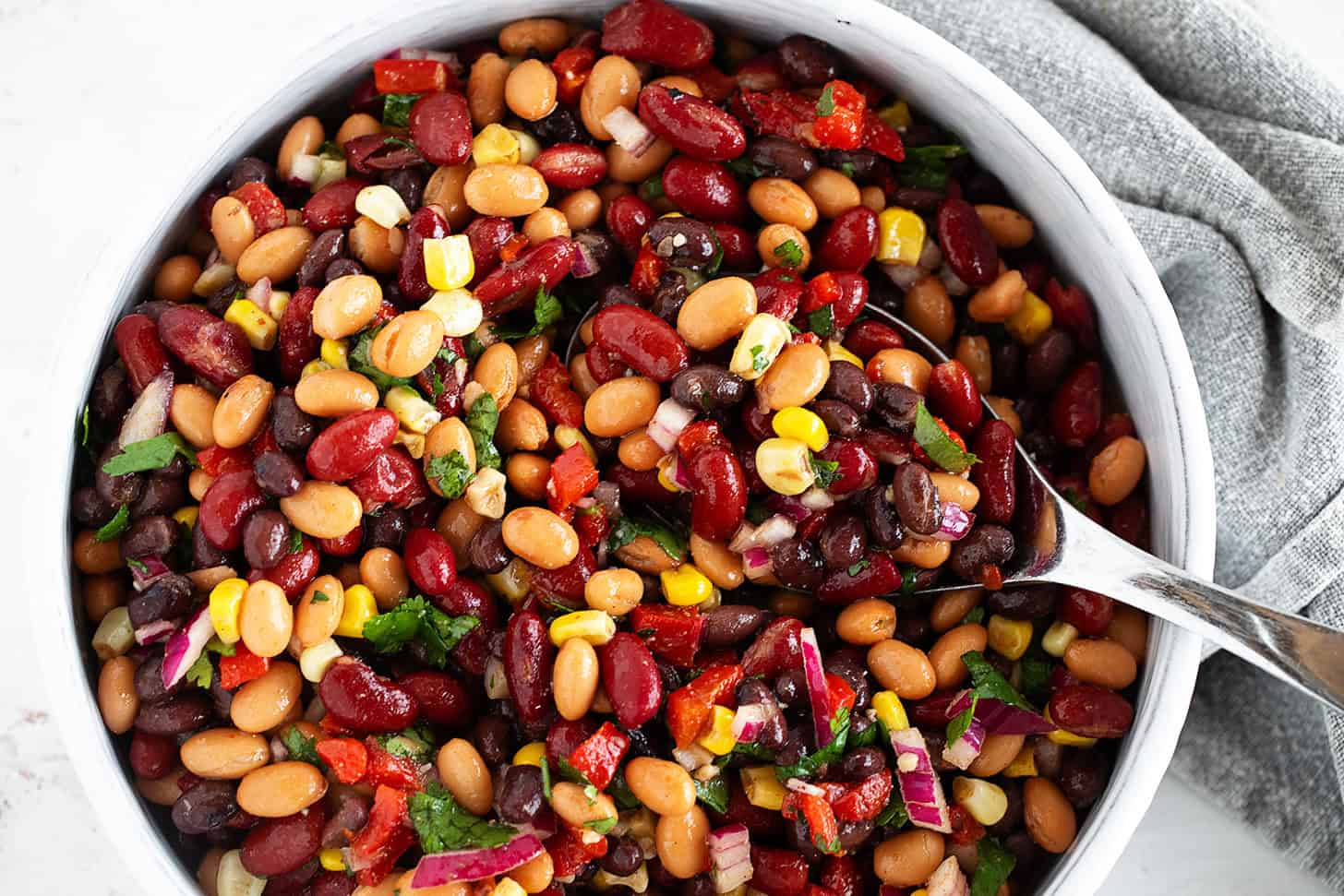 Mexican bean salad in a bowl with a large spoon.