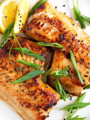 Miso black cod on a serving plate with lemons and green onion.