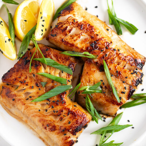 Miso black cod on a serving plate with lemons and green onion.