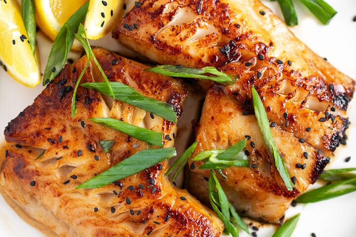 Miso black cod on a serving plate with lemons and green onion.