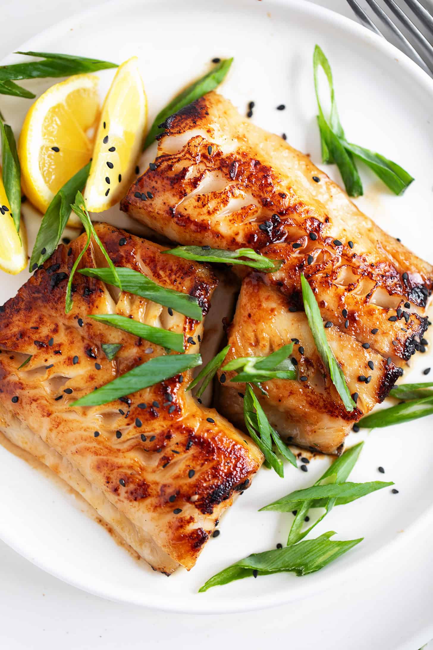 Miso black cod on a serving plate with lemons and green onion.