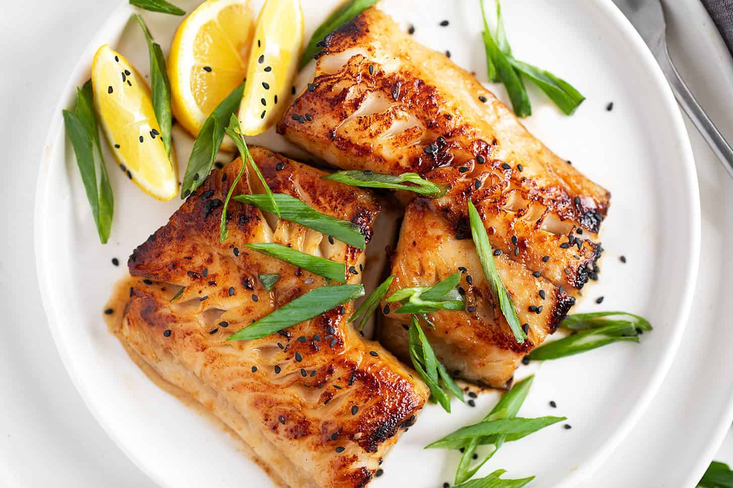 Miso black cod on a serving plate with lemons and green onion.