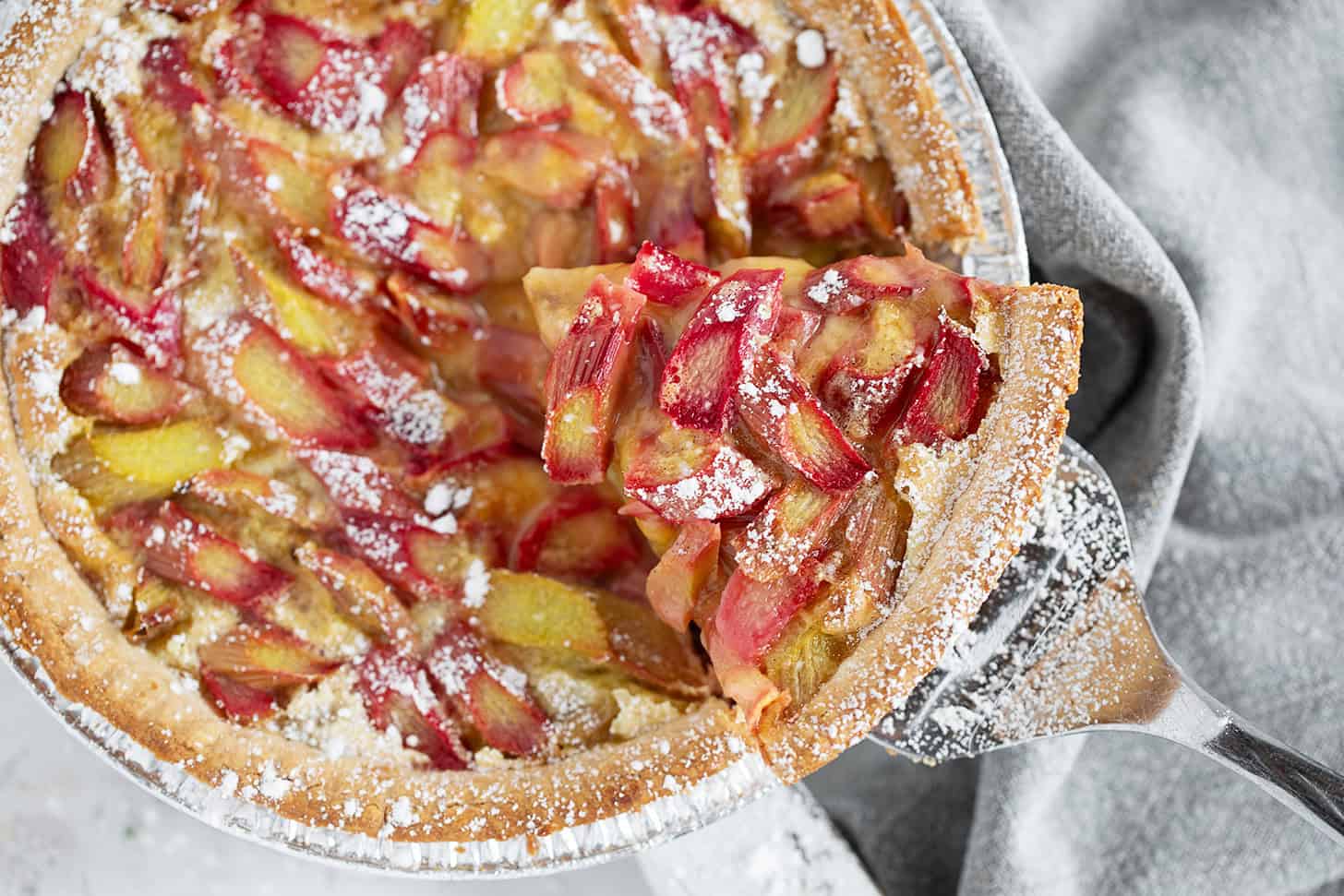 Rhubarb custard pie with a slice on a server.