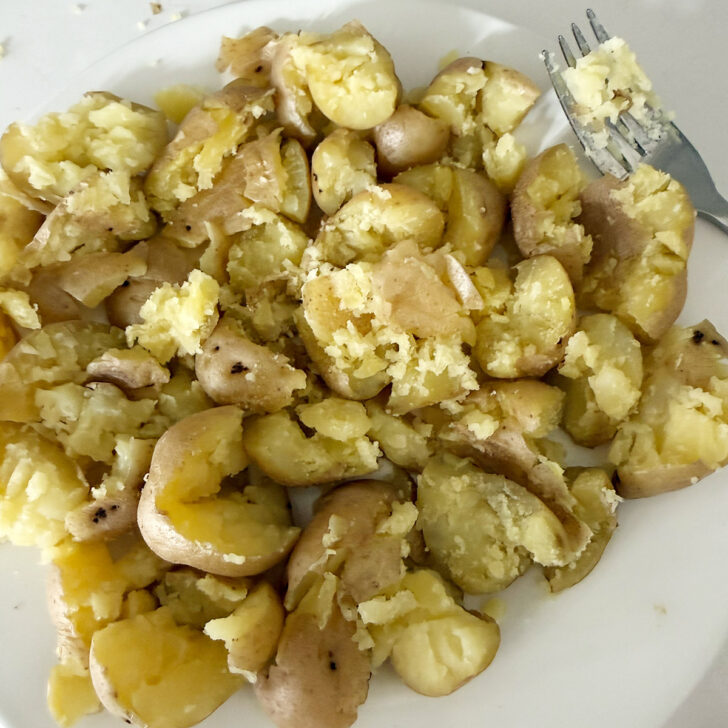 Steamed potatoes smashed with a fork on a plate.