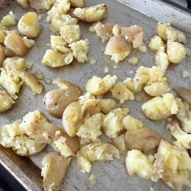 Smashed steamed potatoes on an oiled baking sheet.