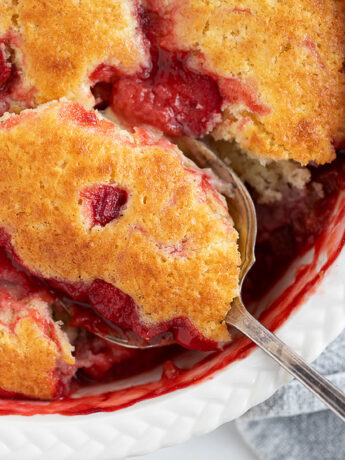 Strawberry rhubarb pudding cake being spooned out.