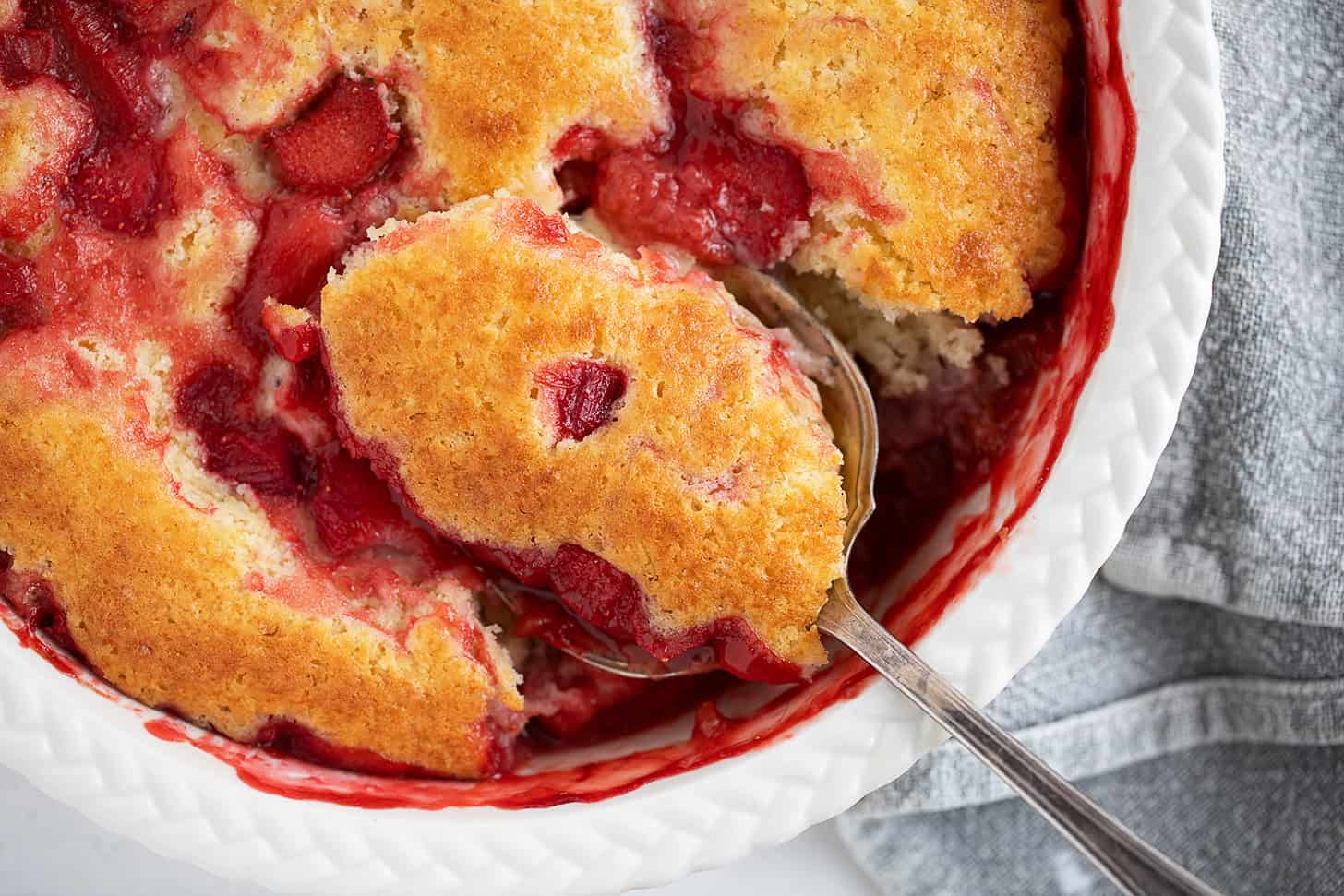 Strawberry rhubarb pudding cake being spooned out.