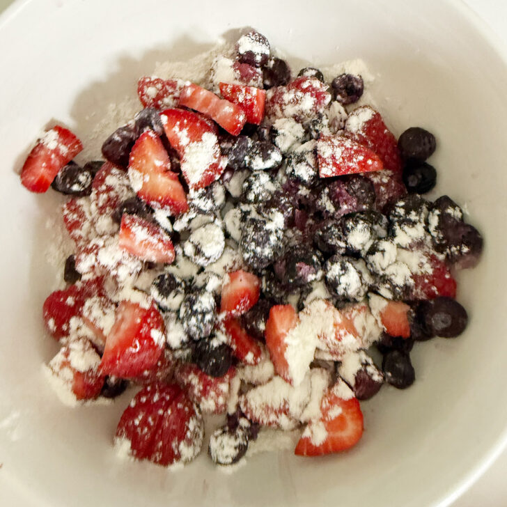 Strawberries, raspberries and blueberries in a bowl with some flour.