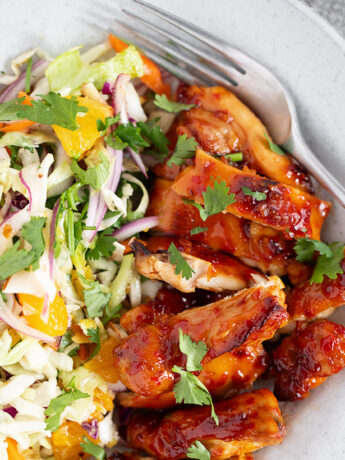 Hot honey chicken thighs with citrus slaw on a dinner plate.
