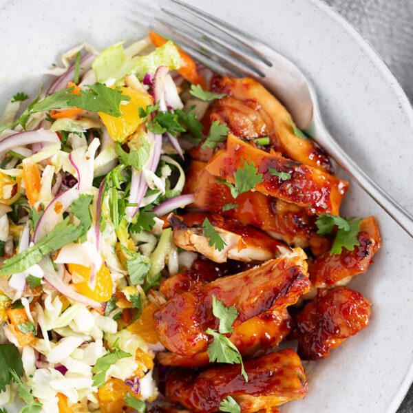 Hot honey chicken thighs with citrus slaw on a dinner plate.
