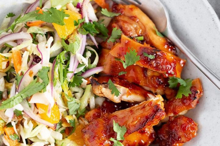 Hot honey chicken thighs with citrus slaw on a dinner plate.