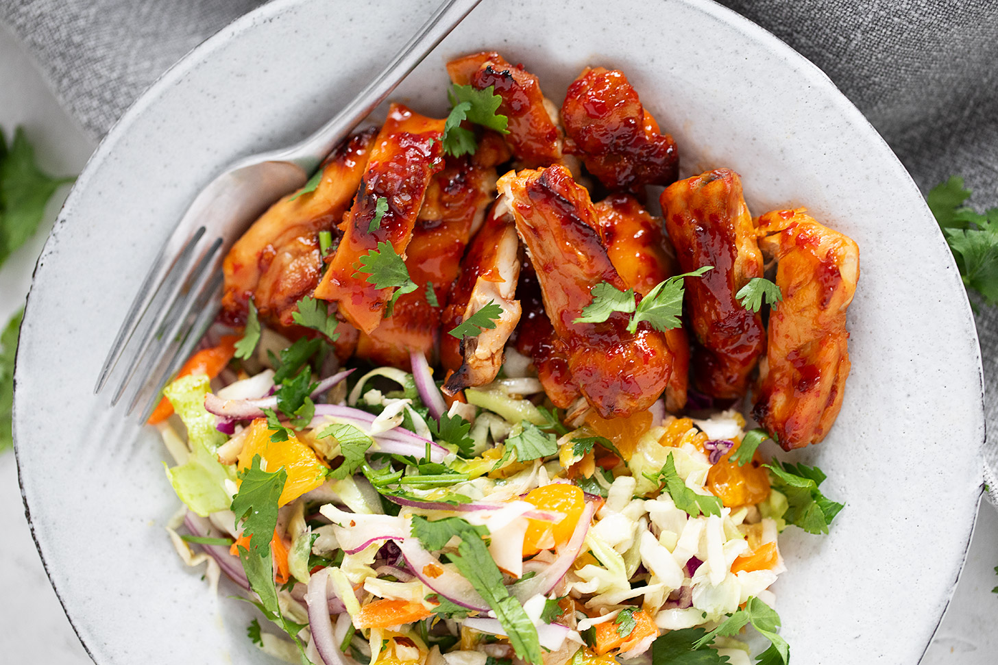 Hot honey chicken thighs with citrus slaw on a dinner plate.