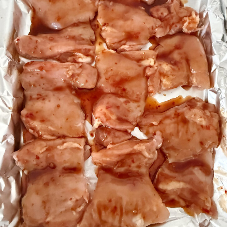Boneless chicken thighs on a baking sheet brushed with the hot honey sauce.