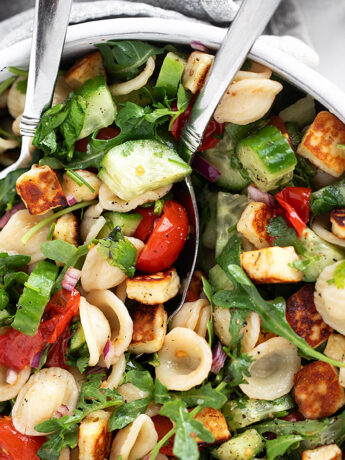 Orecchiette and halloumi salad in a salad bowl with serving spoons.