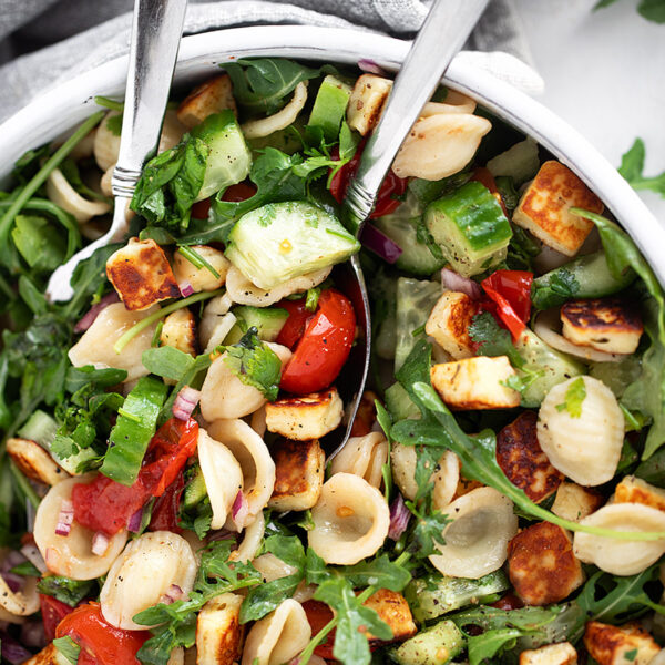 Orecchiette and halloumi salad in a salad bowl with serving spoons.