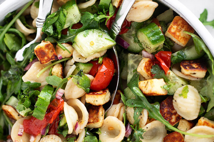 Orecchiette and halloumi salad in a salad bowl with serving spoons.