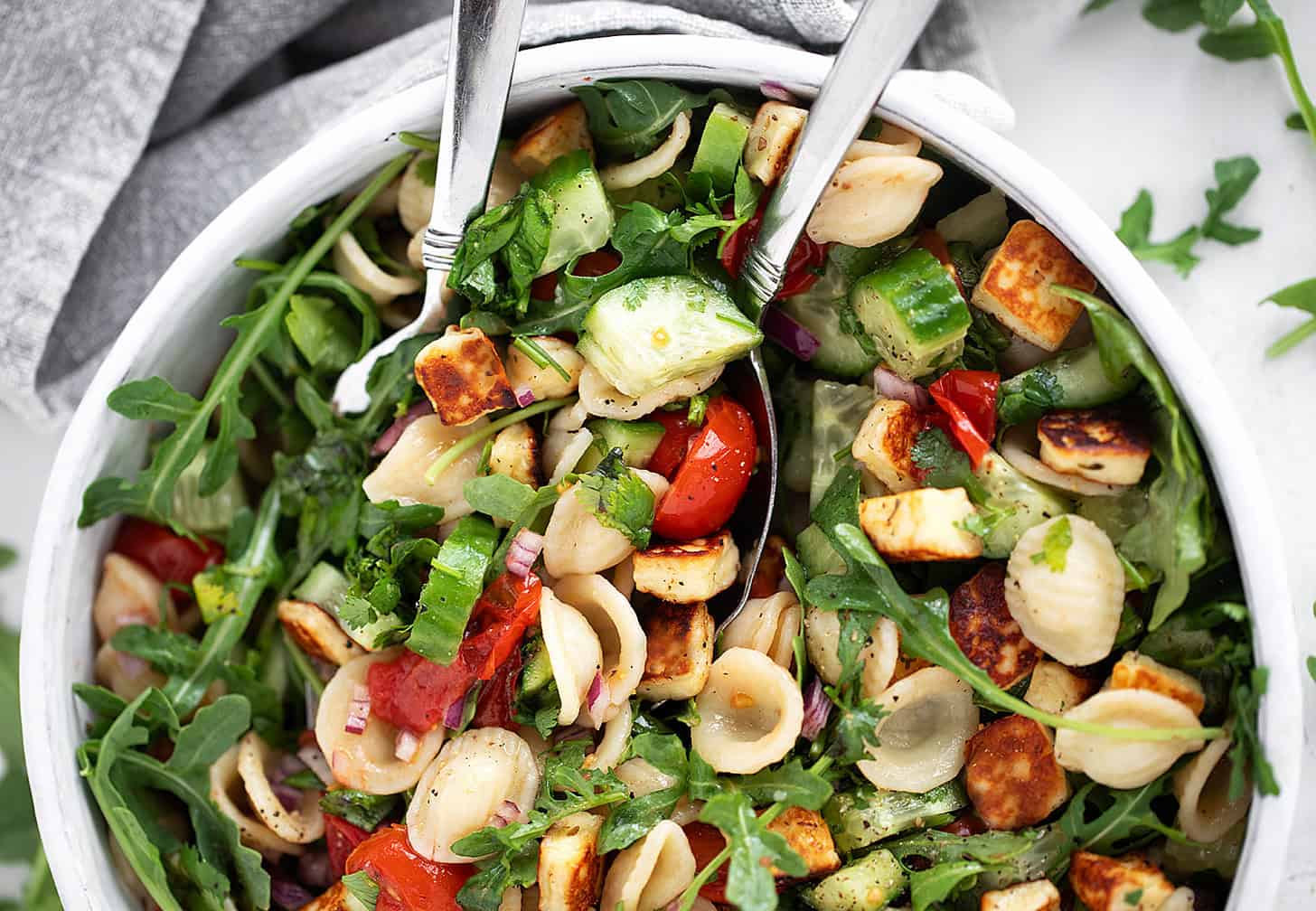 Orecchiette and halloumi salad in a salad bowl with serving spoons.