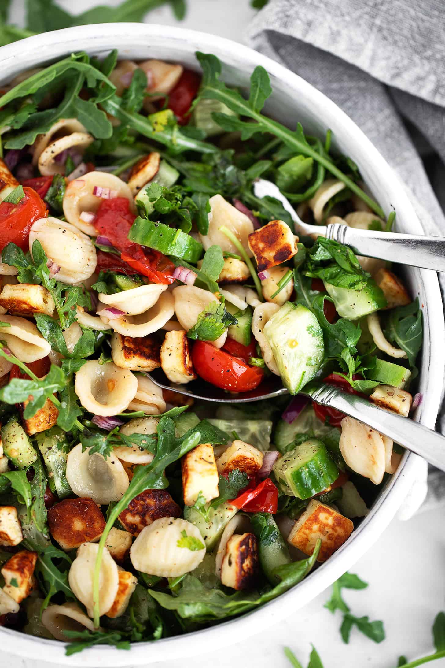 Orecchiette and halloumi salad in a salad bowl with serving spoons.