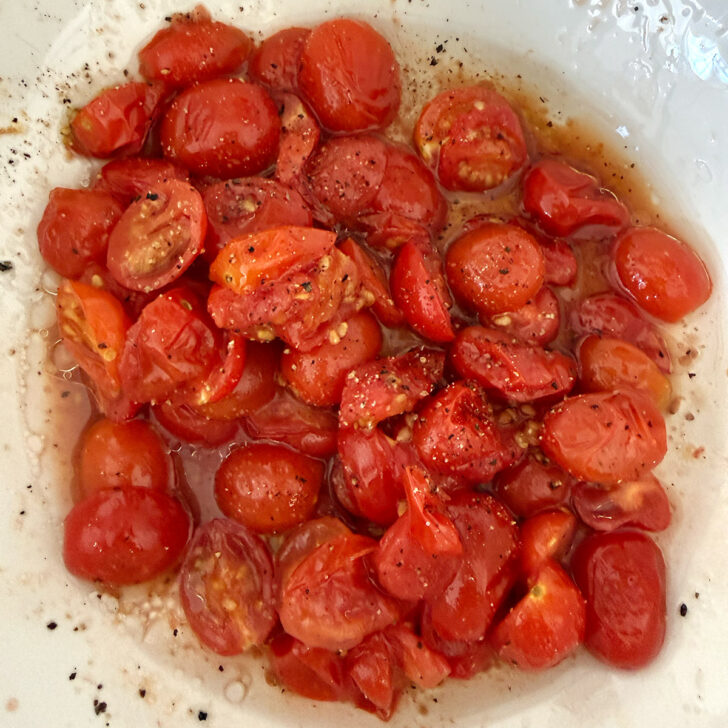 Roasted tomatoes in a bowl with oil and vinegar.
